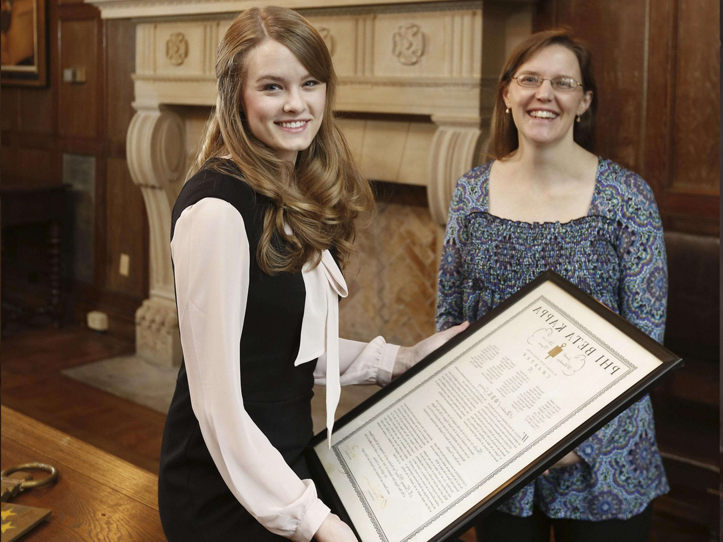 a student holds a Phi Beta Kappa certificate while a professor looks on
