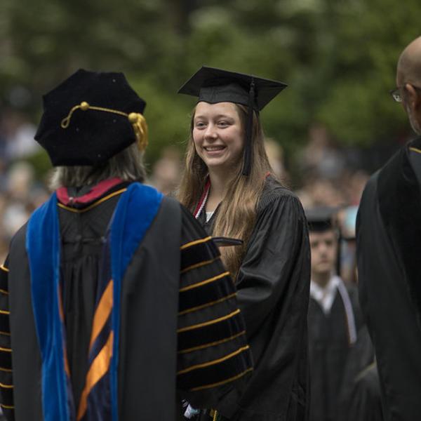 A student in her commencement regalia receives her degree from the president.
