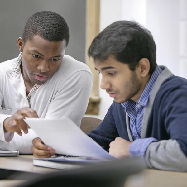A young man helps a fellow student go over an assignment.